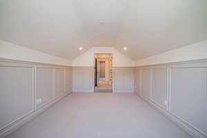 Bonus room with a decorative wall, light carpet, lofted ceiling, and wainscoting