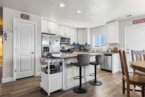Kitchen featuring white cabinets, stainless steel appliances, a kitchen bar, dark wood finished floors, and recessed lighting