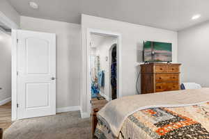 Bedroom with light colored carpet, a spacious closet, arched walkways, and a textured ceiling
