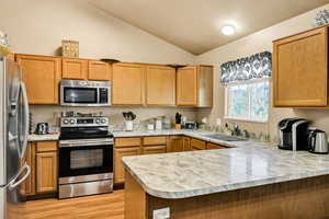 Kitchen with a peninsula, stainless steel appliances, light countertops, lofted ceiling, and light wood-style floors