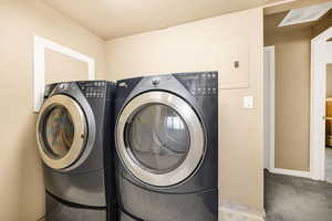 Laundry area featuring electric panel, light carpet, and washer and clothes dryer