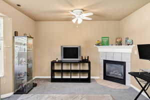 Living area with light carpet, ceiling fan, and a tile fireplace