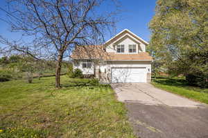 Traditional home with concrete driveway, a front yard, an attached garage, and roof with shingles