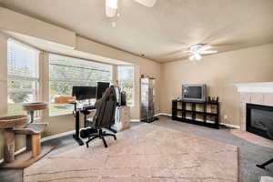 Office area featuring a ceiling fan, light carpet, a textured ceiling, and a tiled fireplace