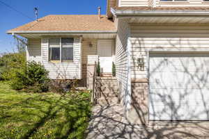 Property entrance featuring roof with shingles, a lawn, and an attached garage
