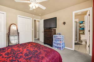 Bedroom featuring light carpet, ensuite bathroom, a ceiling fan, two closets, and light tile patterned flooring