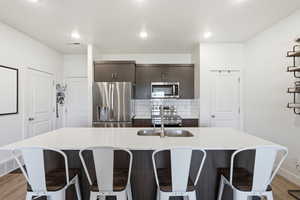 Kitchen featuring light wood-style floors, dark wood finish cabinets, stainless steel appliances, and a kitchen bar