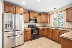 Kitchen with stainless steel appliances, wood finish cabinetry, hanging light fixtures, light countertops, and light tile patterned floors