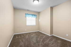 Empty room featuring dark carpet and a textured ceiling
