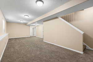 Finished basement with a textured ceiling and dark colored carpet
