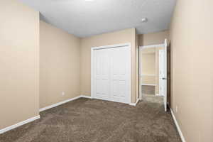 Unfurnished bedroom featuring dark carpet, a closet, and a textured ceiling