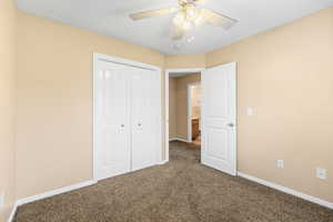 Unfurnished bedroom with dark colored carpet, a closet, and a ceiling fan