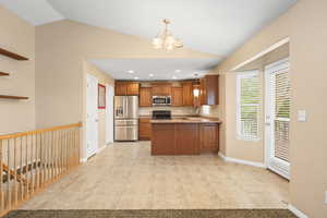 Kitchen with a peninsula, stainless steel appliances, wood finish cabinets, light tile patterned floors, and a chandelier