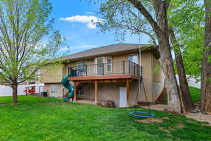 Back of house with a wooden deck, stucco siding, a lawn, and a patio
