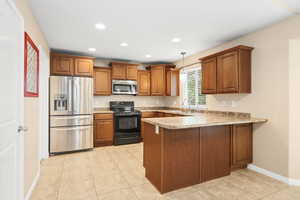 Kitchen with stainless steel appliances, a peninsula, wood finish cabinets, light tile patterned flooring, and pendant lighting