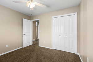 Unfurnished bedroom with dark carpet, a closet, and a ceiling fan