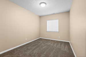 Unfurnished room featuring a textured ceiling and dark colored carpet