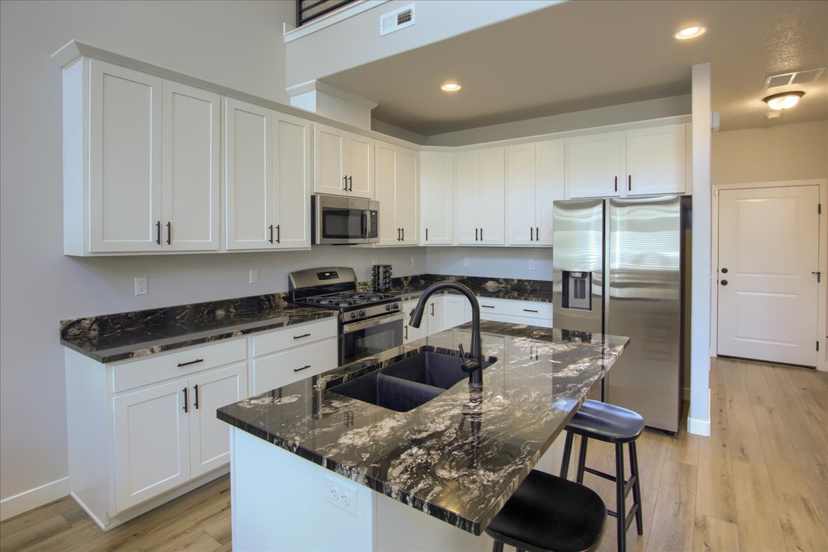 Kitchen with stainless steel appliances, white cabinets, dark granite counters, a kitchen island with sink, and a kitchen breakfast bar