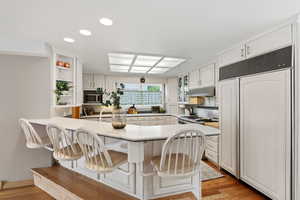 Kitchen with a kitchen bar, paneled built in fridge, a peninsula, recessed lighting, and glass insert cabinets