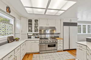 Kitchen featuring light countertops, paneled fridge, range with two ovens, white cabinetry, and glass insert cabinets