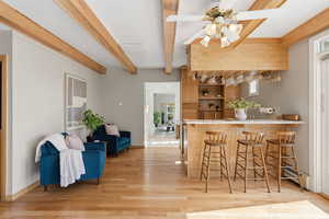 Kitchen featuring light wood-style flooring, a ceiling fan, a kitchen bar, a baseboard radiator, and beam ceiling