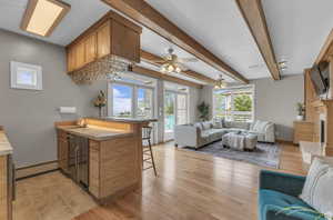 Wet bar featuring open floor plan, a peninsula, a breakfast bar, light countertops, and wood finish cabinetry