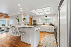 Kitchen with white cabinetry, a peninsula, light wood-type flooring, recessed lighting, and a kitchen bar