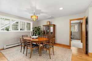 Dining room with light wood-style floors, a baseboard heating unit, suspended lighting, and baseboard heating