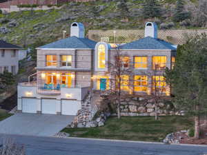 Front of property featuring a chimney, a balcony, a lawn, concrete driveway, and an attached garage