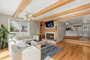 Living room with light wood finished floors, beamed ceiling, a ceiling fan, a high end fireplace, and baseboard heating