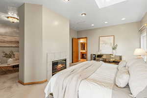 Bedroom featuring light colored carpet, a fireplace, a skylight, connected bathroom, and recessed lighting