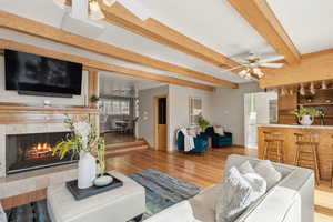 Living area featuring ceiling fan, light wood-style flooring, a tile fireplace, and beamed ceiling