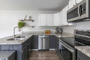 Kitchen featuring stainless steel appliances, a peninsula, light stone counters, dual tone cabinets, and dark wood-style floors
