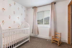 Bedroom with dark colored carpet, a crib, and wallpapered walls