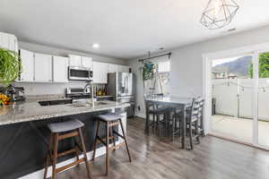 Kitchen featuring a kitchen breakfast bar, stainless steel appliances, light stone countertops, dark wood-type flooring, and a peninsula