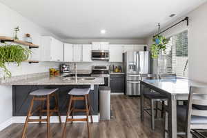 Two tone kitchen with a kitchen breakfast bar, a peninsula, stainless steel appliances, light stone counters, and dual tone cabinets