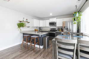 Kitchen with a breakfast bar, a peninsula, two tone cabinetry, stainless steel appliances, and light stone counters