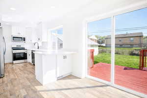 Kitchen featuring stainless steel appliances, a peninsula, light wood-style flooring, white cabinets, and recessed lighting