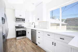 Kitchen featuring stainless steel appliances, white cabinets, light wood-style floors, light stone counters, and backsplash