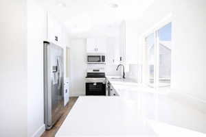 Kitchen featuring stainless steel appliances, white cabinets, light wood finished floors, light stone counters, and tasteful backsplash