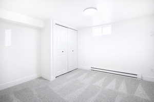 Unfurnished bedroom with light carpet, a baseboard heating unit, and a closet