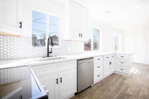 Kitchen featuring dark wood finished floors, white cabinetry, stainless steel dishwasher, light stone counters, and a peninsula
