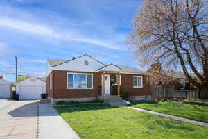 Bungalow-style home with a garage, brick siding, an outdoor structure, and a chimney