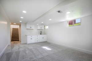 Indoor wet bar featuring white cabinetry, light carpet, recessed lighting, and light countertops