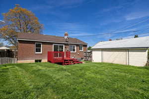 Back of house featuring a deck, a chimney, a fenced backyard, brick siding, and an outdoor structure