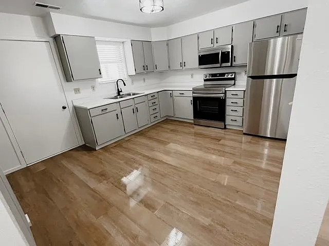 Kitchen with gray cabinets, light countertops, stainless steel appliances, and light wood-type flooring