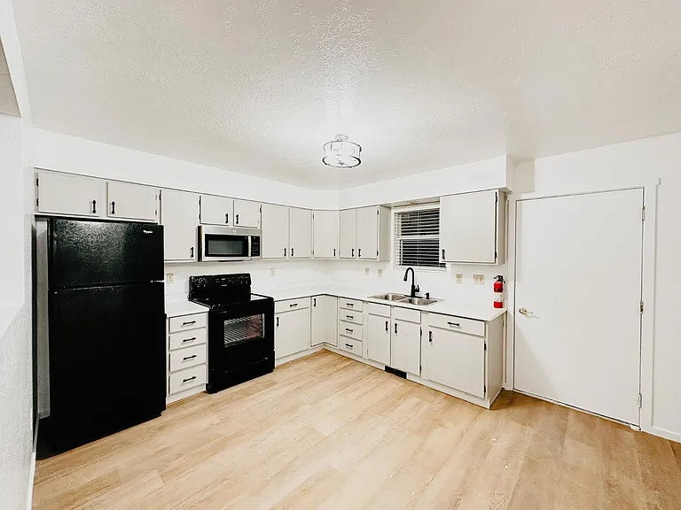 Kitchen with light countertops, black appliances, a textured ceiling, and light wood-type flooring