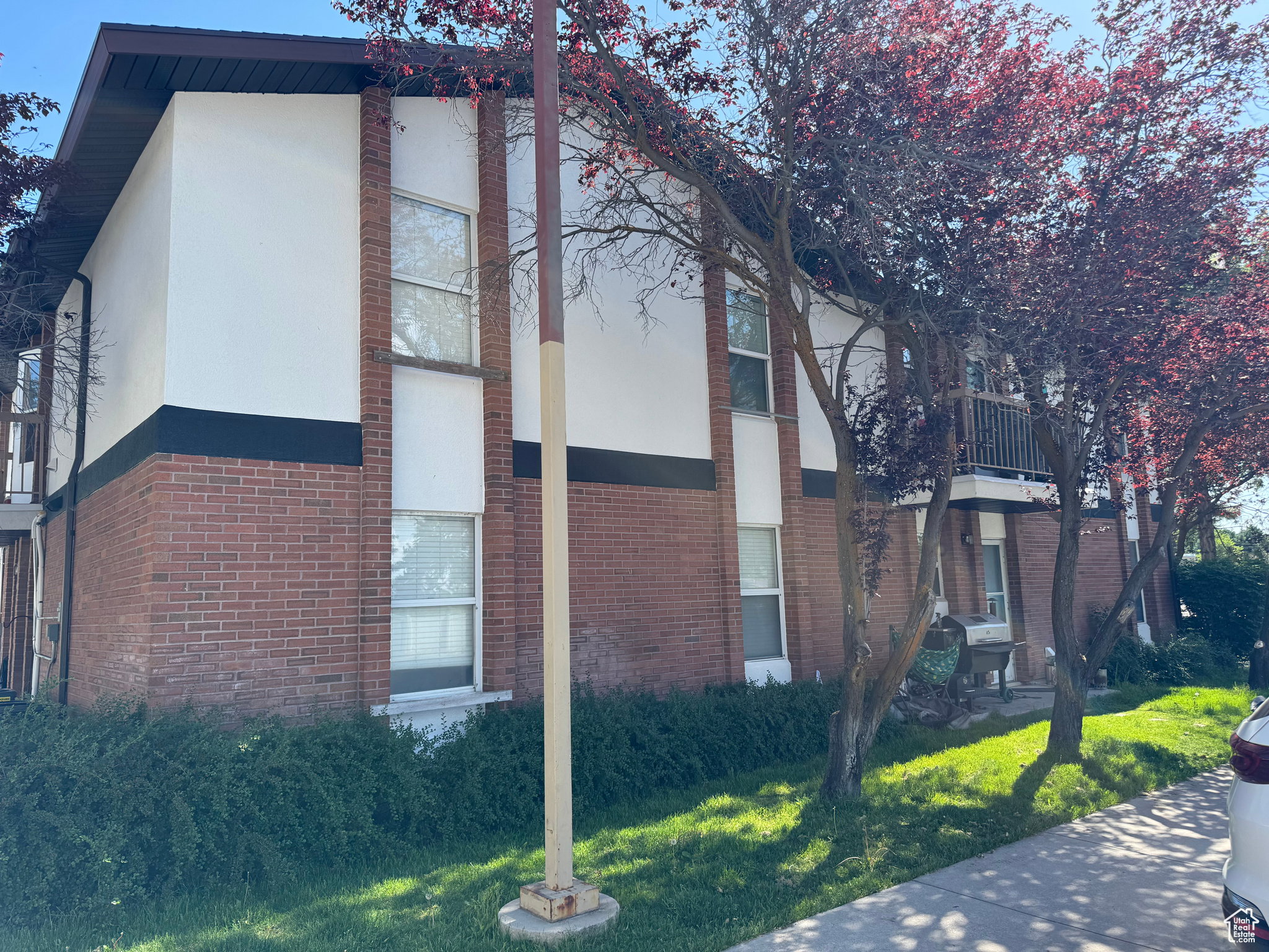 View of property exterior with stucco siding, a balcony, brick siding, and a yard