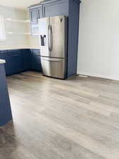 Kitchen with stainless steel fridge, blue cabinets, light countertops, open shelves, and healthy amount of natural light