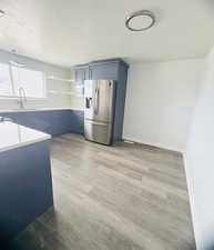 Kitchen featuring stainless steel fridge with ice dispenser, light wood-style floors, blue cabinetry, open shelves, and a textured ceiling